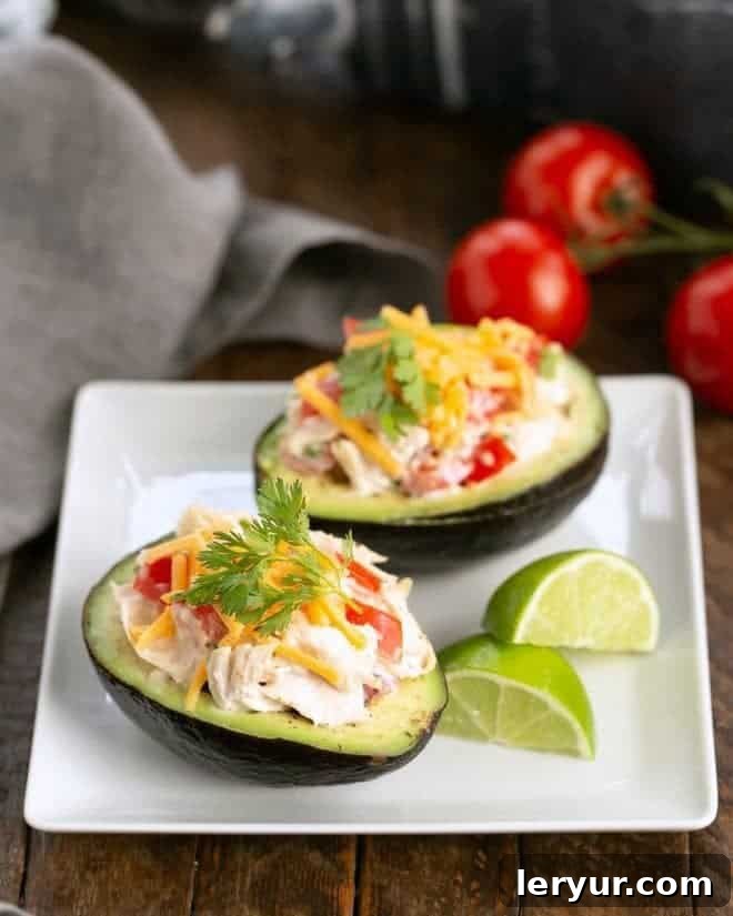 Two halves of Southwestern Chicken Stuffed Avocados, generously filled and topped, are arranged on a square white plate, accompanied by vibrant lime wedges. This image emphasizes the freshness and zesty appeal of the dish.