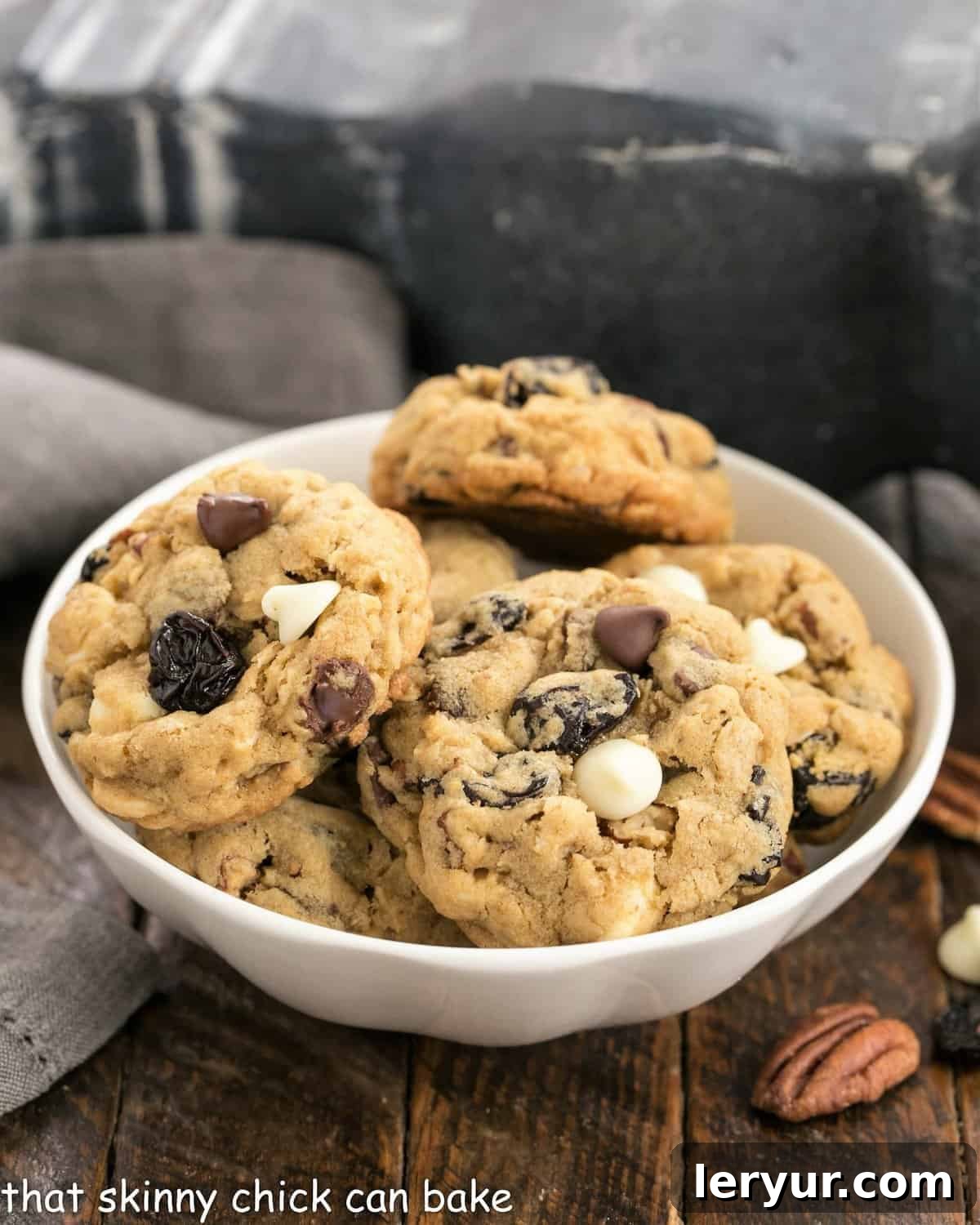 Chewy Oatmeal Cookies with Dark and White Chocolate Chunks, toasted pecans and dried cherries! Perfect for after school snacks, lunch boxes and an after dinner treat! Chewy Oatmeal Cookies in a small white ceramic bowl.