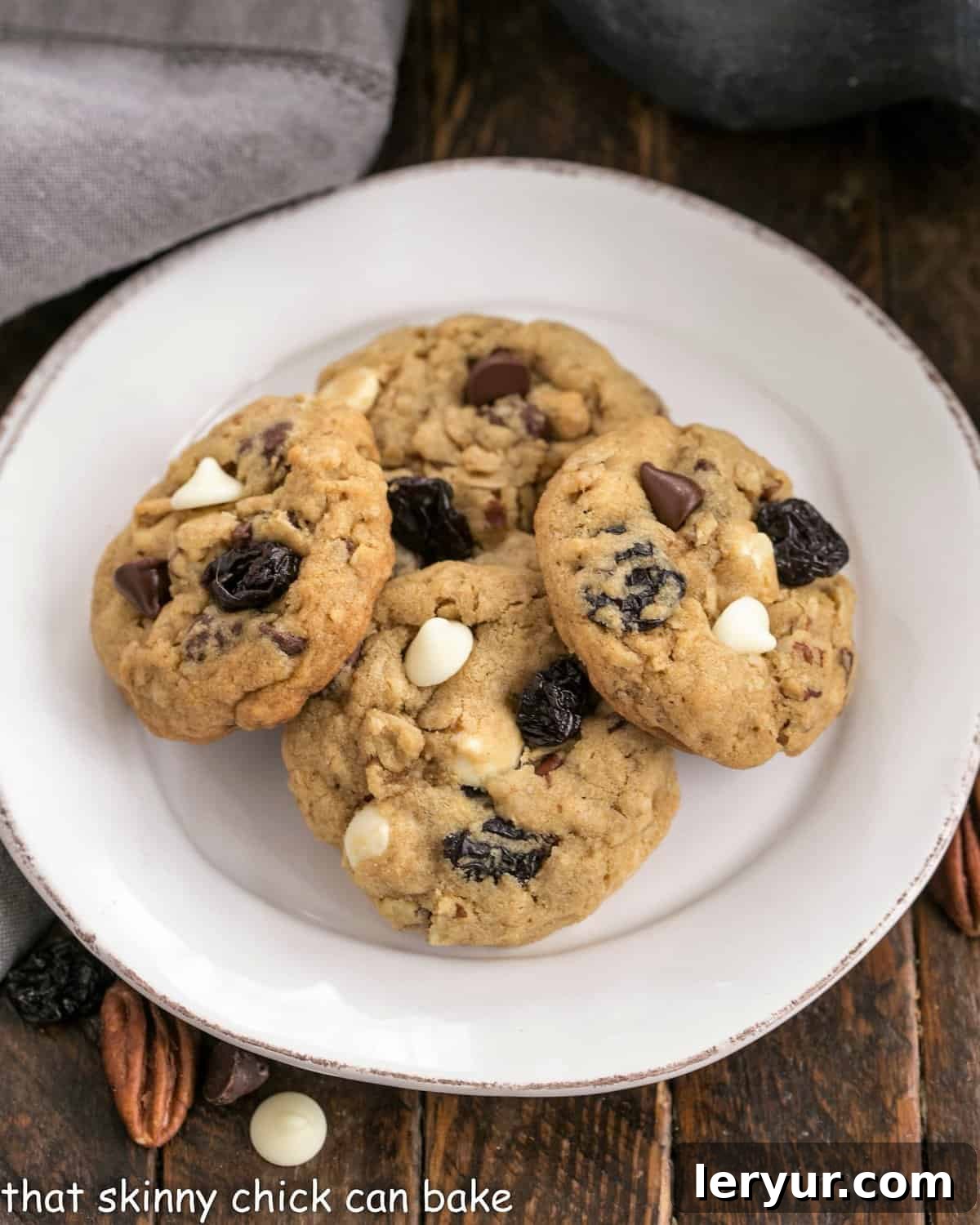 Easy Oatmeal Cookies with Dark and White Chocolate Chunks, toasted pecans and dried cherries! Perfect for after school snacks, lunch boxes and an after dinner treat! Overhead view of Chewy oatmeal cookies on a white plate.
