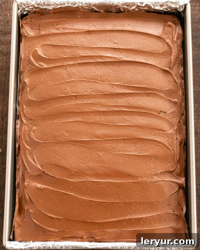 Velvet Night Snack Cakes 14 Chocolate buttercream frosting being spread evenly over the cooled Black Magic Snack Cake, creating a smooth and delicious top layer.