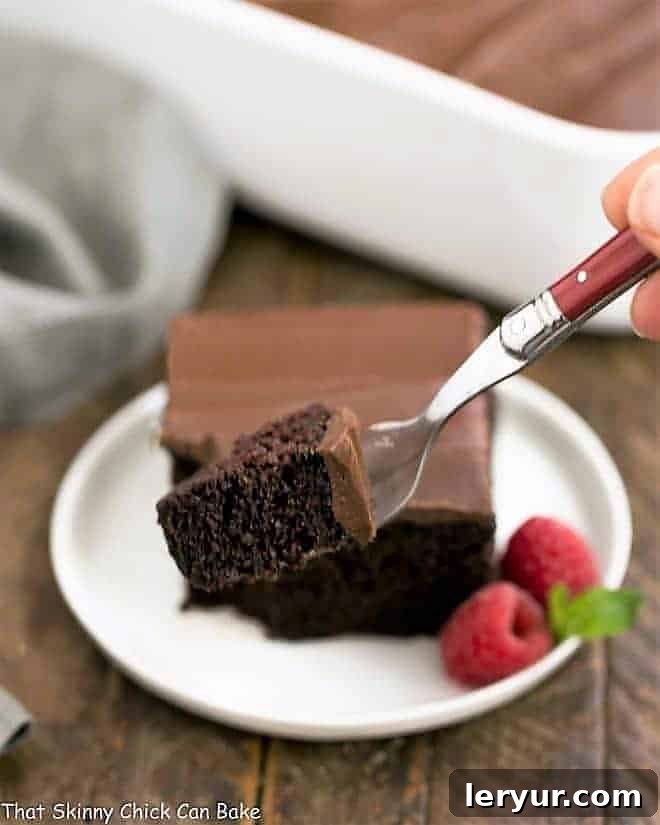 Velvet Night Snack Cakes 16 A tempting slice of Black Magic Snack Cake on a round plate with a red fork, showing the moist interior and generous chocolate frosting, with a small piece of cake in the foreground.