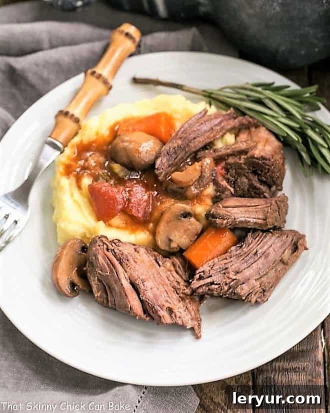 Oven Pot Roast Recipe with Mushrooms, Tomatoes & Red Wine - marvelous comfort food with an exquisite depth of flavor! Pot Roast with Mushrooms, Tomatoes & Red Wine on a white plate with mashed potatoes and a sprig of rosemary.