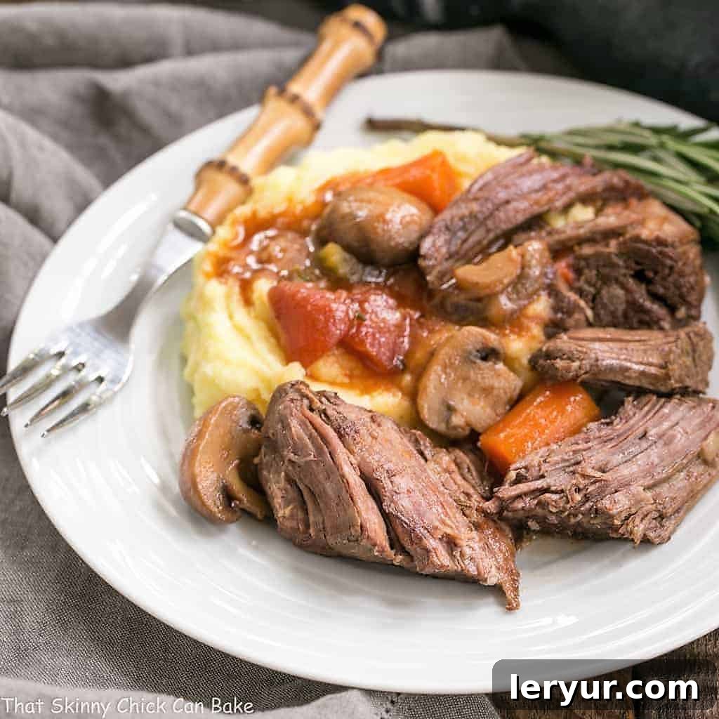 Pot Roast in oven Recipe - This is one unforgettable beef pot roast with an amazing depth of flavor! Pot Roast in Oven with Mushrooms, Tomatoes & Red Wine on a white ceramic plate with a bamboo handled fork.