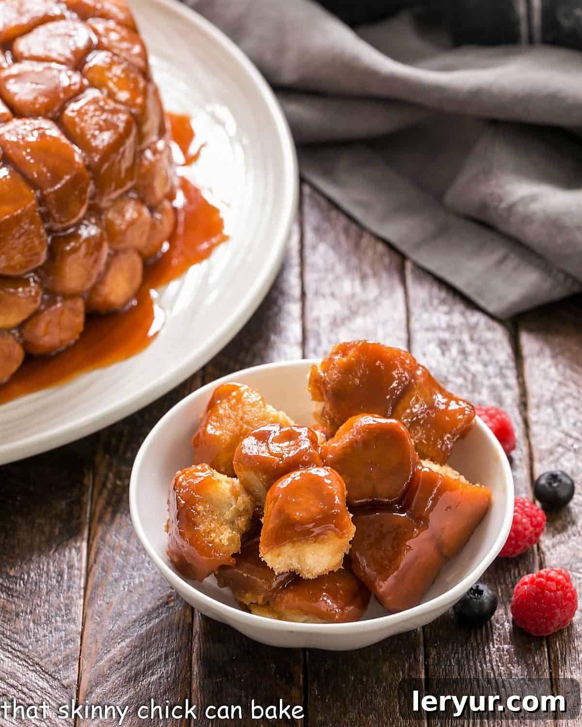 Monkey bread in a white ceramic bowl, showing smaller, quartered roll dough balls coated in a rich caramel topping.