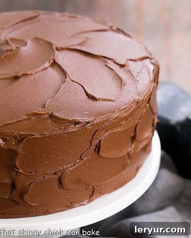 Chocolate Layer Cake with Ganache on a white ceramic cake stand, showcasing rich chocolate frosting and white ganache filling.