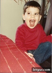 The birthday boy as a child in a red shirt and jeans with a big smile, looking excited for his cake.
