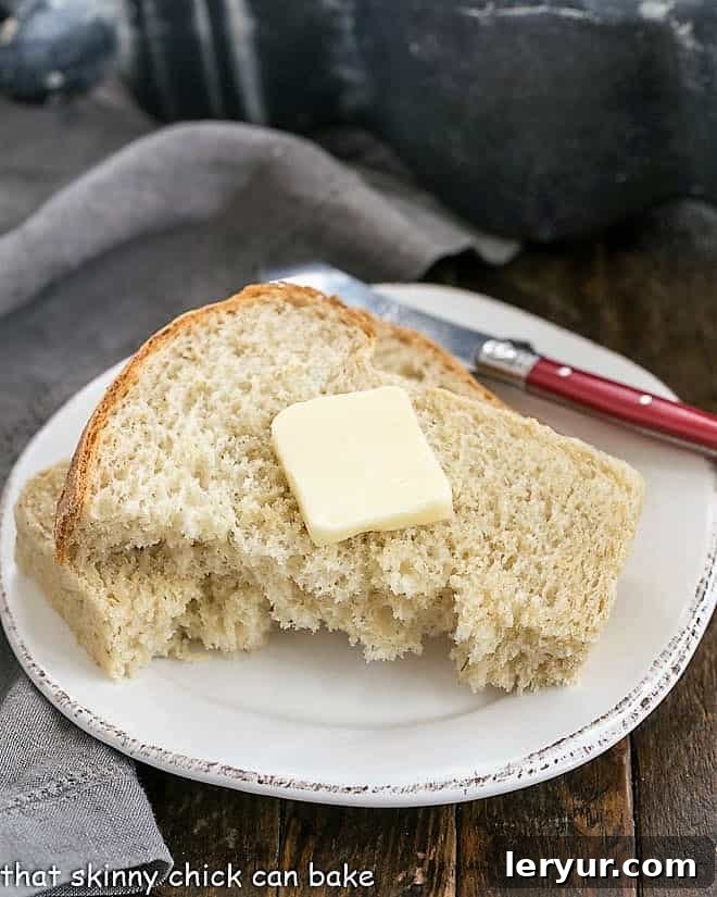 Oatl Bread - a sweet, hearty yeast bread recipe flavored with a touch of brown sugar A torn slice of homemade oatmeal bread, topped with a generous pat of butter, resting on a round white plate with a red-handled butter knife beside it.