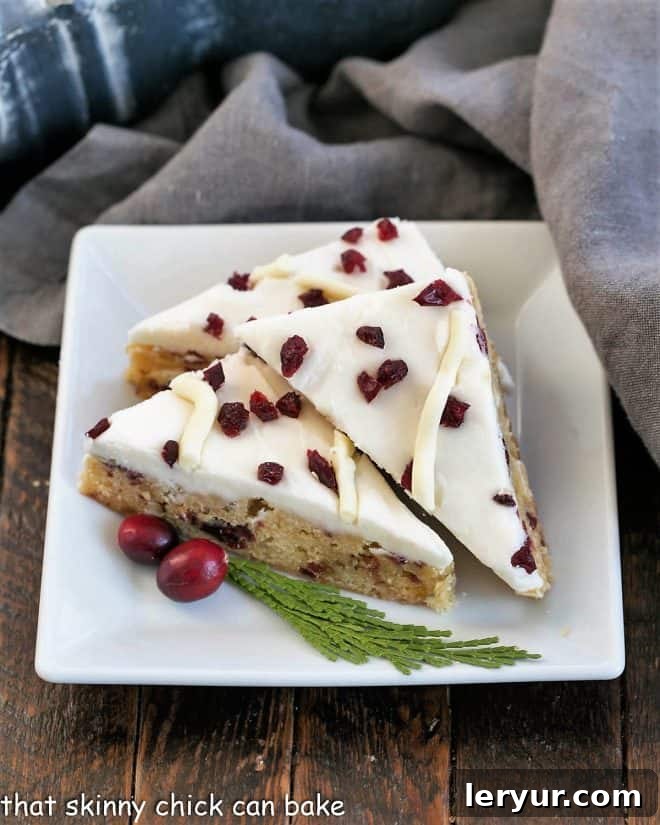 Three beautifully frosted Cranberry Bliss Bars on a square white plate, ready to be enjoyed.