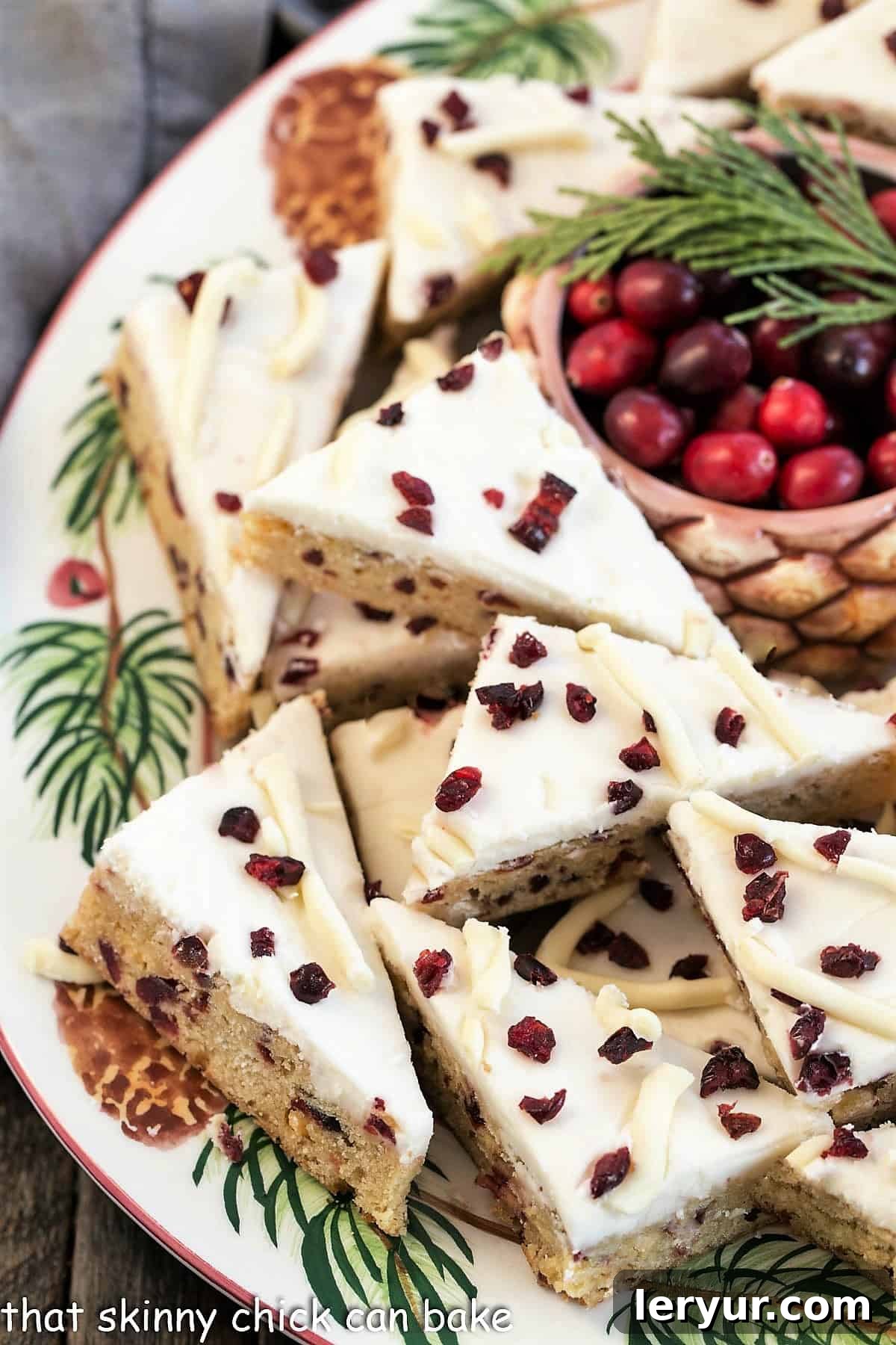 A festive tray of homemade Starbucks Cranberry Bliss Bars, garnished with fresh cranberries and evergreen sprigs, ready for serving.