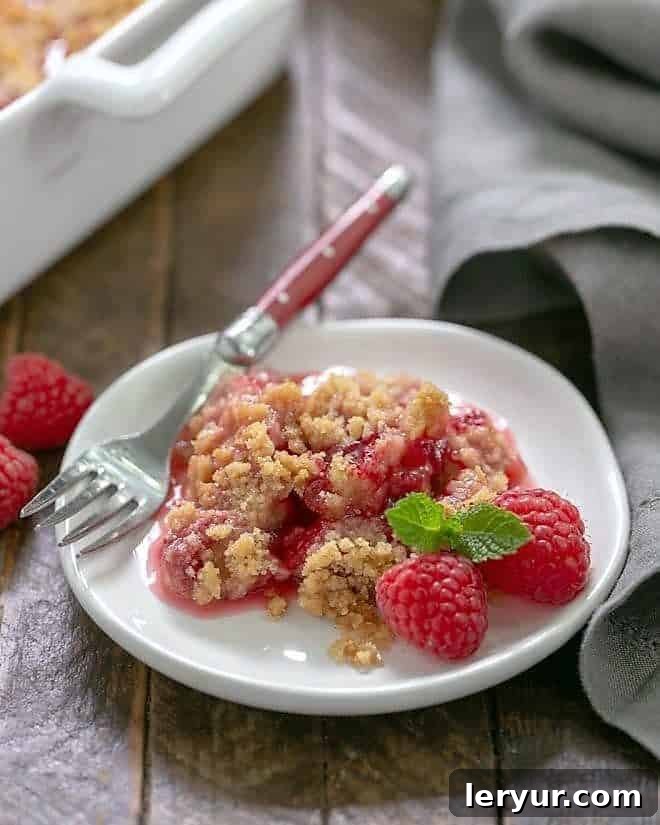 Fresh Raspberry Crisp portion on a small white plate garnished with fresh raspberries and mint, ready to be enjoyed.