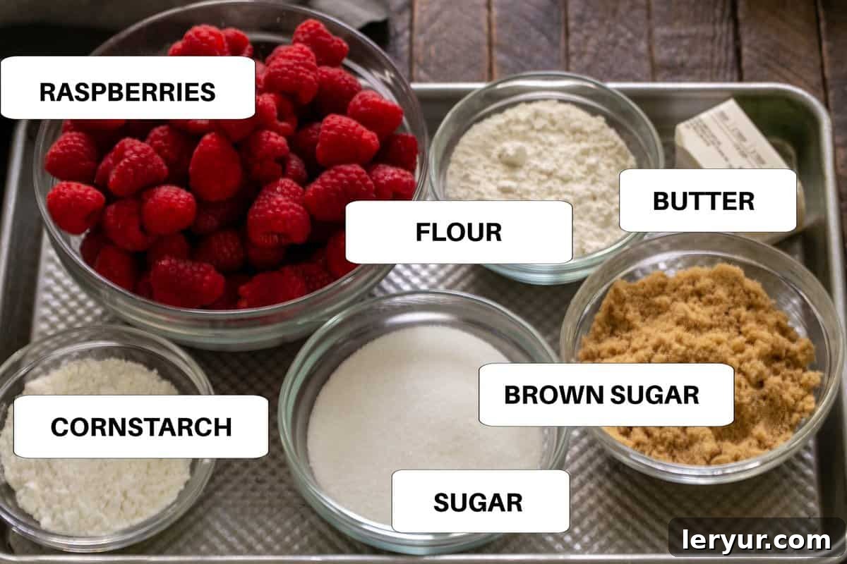 Labeled ingredients for raspberry crisp laid out neatly on a metal sheetpan, showing fresh raspberries, flour, sugars, and butter.