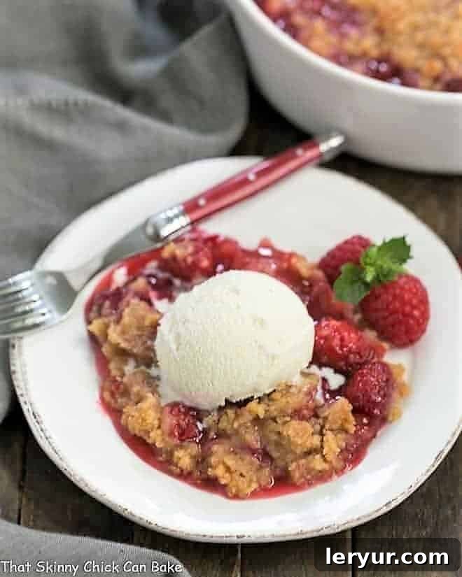 Overhead view of Fresh Raspberry Crisp on a white dessert plate with a scoop of vanilla ice cream and fresh berries, garnished with mint.