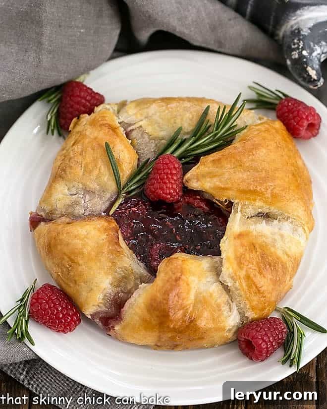 Baked Brie with Raspberries - a spectacular appetizer with creamy brie, a raspberry, rosemary topping and a flaky puff pastry crust! Overhead view of Raspberry Baked Brie en Croute, golden and inviting.