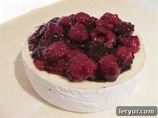 Baked Brie with Raspberries - a spectacular appetizer with creamy brie, a raspberry, rosemary topping and a flaky puff pastry crust! Brie with berry topping on a sheet of parchment paper, ready to be wrapped.