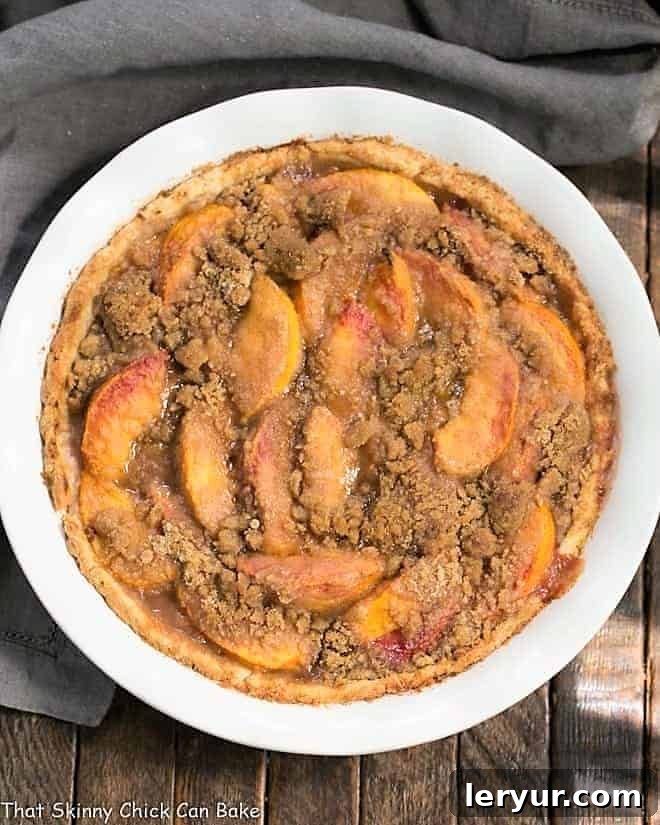 Overhead view of an Easy Peach Crumb Pie in a white pie plate, showcasing its golden crumb topping and the promise of juicy peach filling.