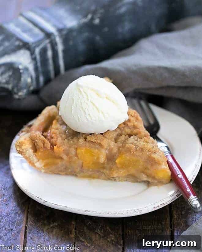 A perfectly sliced piece of Easy Peach Crumb Pie, topped with a scoop of vanilla ice cream, served on a round white plate.