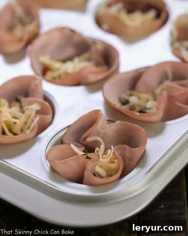 Savory Ham and Egg Cups 2 Egg Muffins in ham cups nestled in a muffin tin, ready to be baked in the oven.