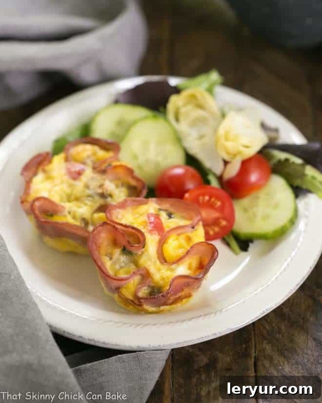 Egg Muffins in Ham Cups - a scrumptious, portable omelet Egg Muffins in Ham Cups served alongside a fresh green salad on a small white plate, making for a complete meal.