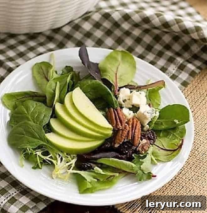 Close-up view of a serving of Winter Salad with Apples, Pecans, Blue Cheese and Dried Cherries on a small white plate, showing the vibrant colors and textures of the ingredients.