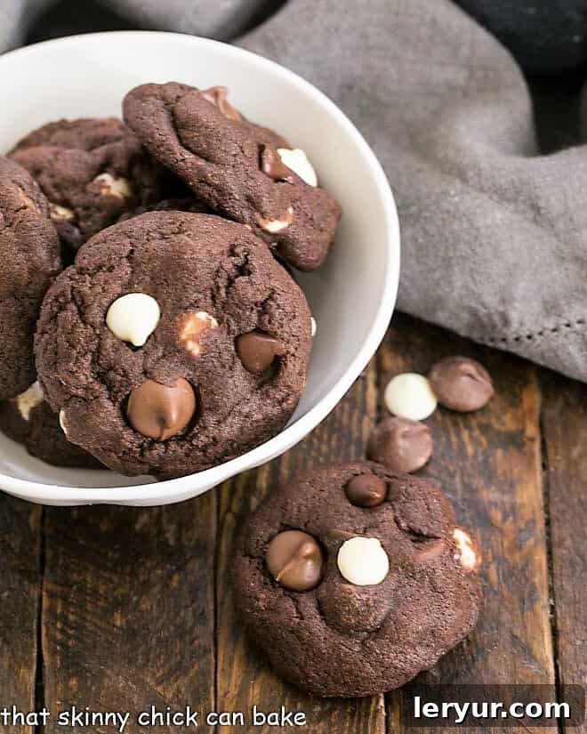 An overhead view of a bowl filled with perfectly baked Quadruple Chocolate Cookies, with one cookie removed, showcasing its rich texture.