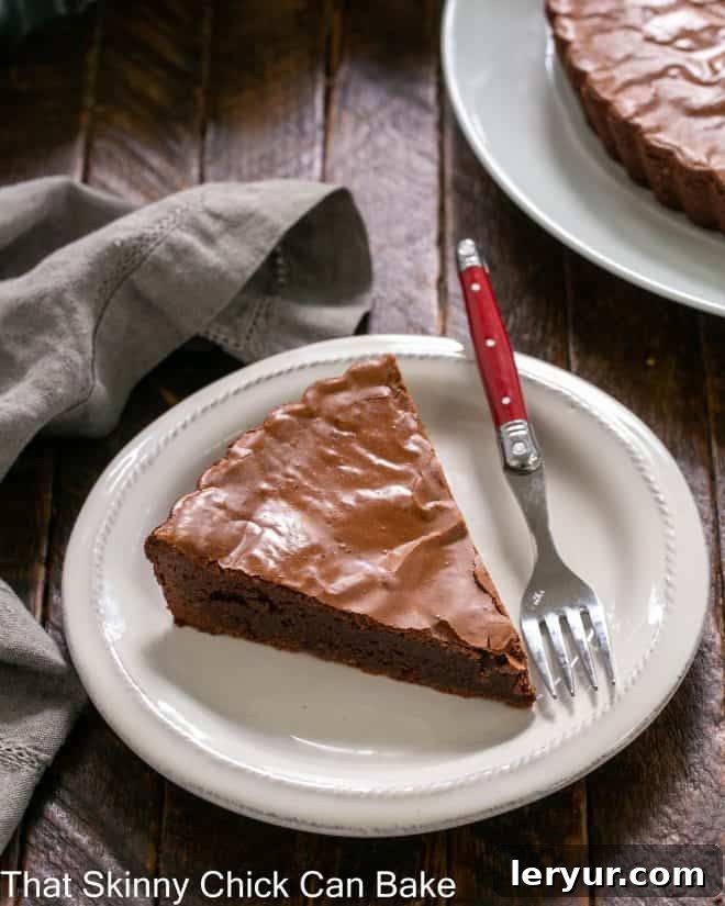 Decadent Chocolate Brownie Tart 2 Ungarnished slice of brownie pie on a white dessert plate with a red handled fork.