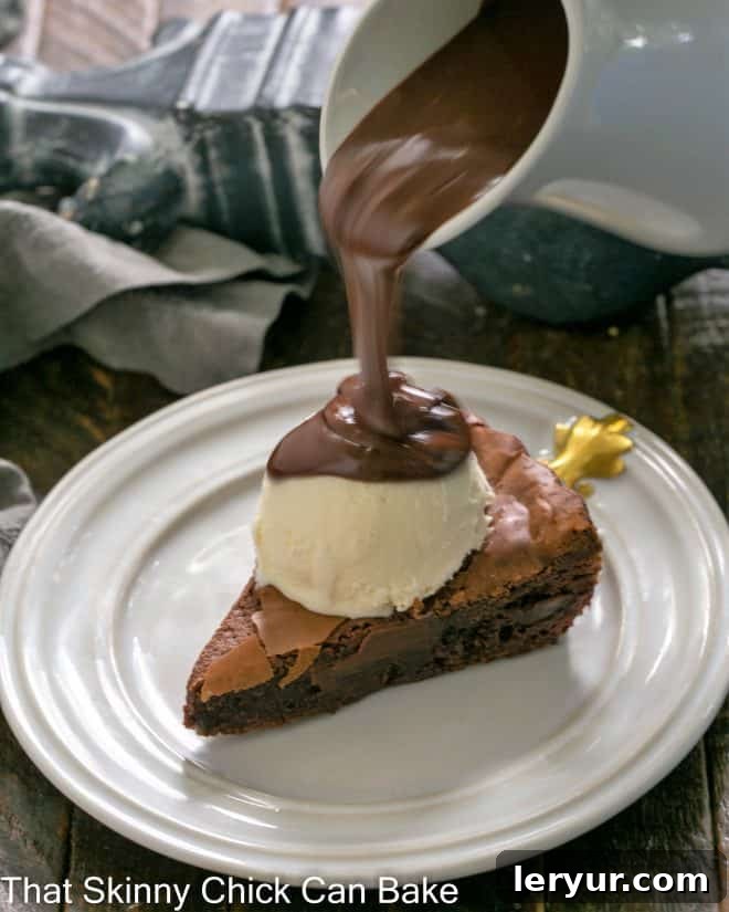 Decadent Chocolate Brownie Tart 3 Slice of brownie tart topped with a scoop of vanilla ice cream with chocolate sauce pouring out from a white ceramic pitcher.
