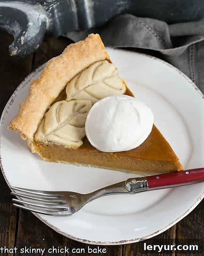 The Best Homemade Pumpkin Pie: An elevated classic perfect for Thanksgiving. Overhead view of a Pumpkin Pie slice garnished with whipped cream, showcasing its creamy texture and golden crust.