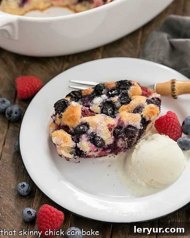 Easy Mixed Berry Cobbler - a simple, delicious dessert made with seasonal berries A serving of Easy Mixed Berry Cobbler on a white dessert plate with a scoop of ice cream and fresh berries, ready to be enjoyed.
