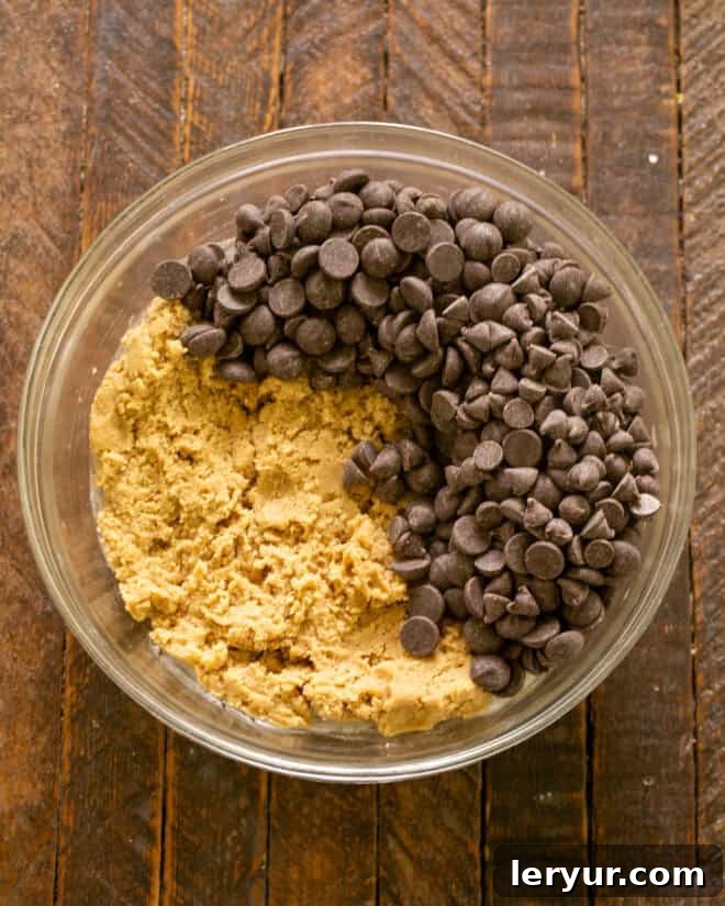 Dangerously Delicious Chocolate Chip Cookies 8 A close-up of the cookie dough in a mixing bowl, now studded generously with a mixture of semisweet and bittersweet chocolate chips, ready for a final gentle stir.