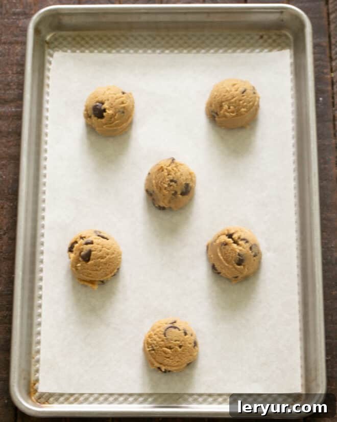 Dangerously Delicious Chocolate Chip Cookies 9 Scoops of chocolate chip cookie dough, perfectly portioned and rolled into neat balls, resting on a parchment-lined baking sheet, prepared for chilling and baking.