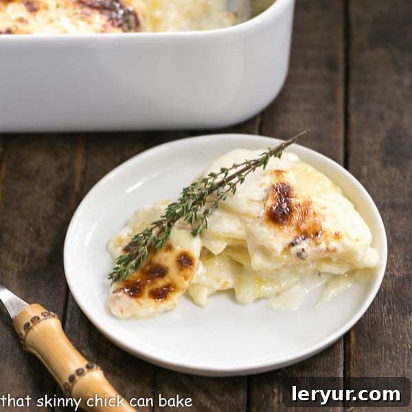 French Potato Gratin - A exquisite creamy cheesy potato casserole kissed with garlic, thyme and topped with Gruyere cheese! Ideal for any celebration. A close-up of a serving of French Potato Gratin on a white round plate, with a bamboo-handled fork, highlighting the golden cheesy crust.