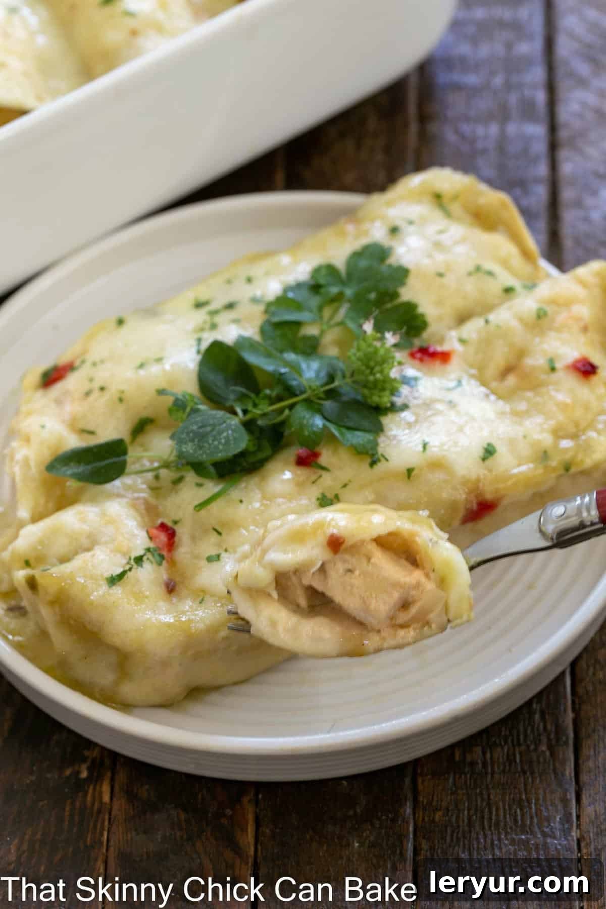 Creamy Chicken Enchiladas - an easy delicious weeknight meal! Creamy chicken enchilada on a white plate with a casserole dish in the background.