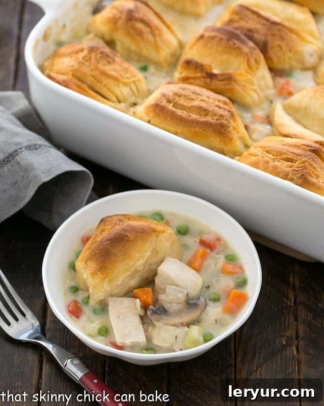 Homemade Chicken Pot Pie with Flaky Biscuits - The ultimate comfort food dish A shallow bowl of golden-brown chicken pot pie, topped with flaky biscuits, resting in front of the full casserole dish, ready to be served.