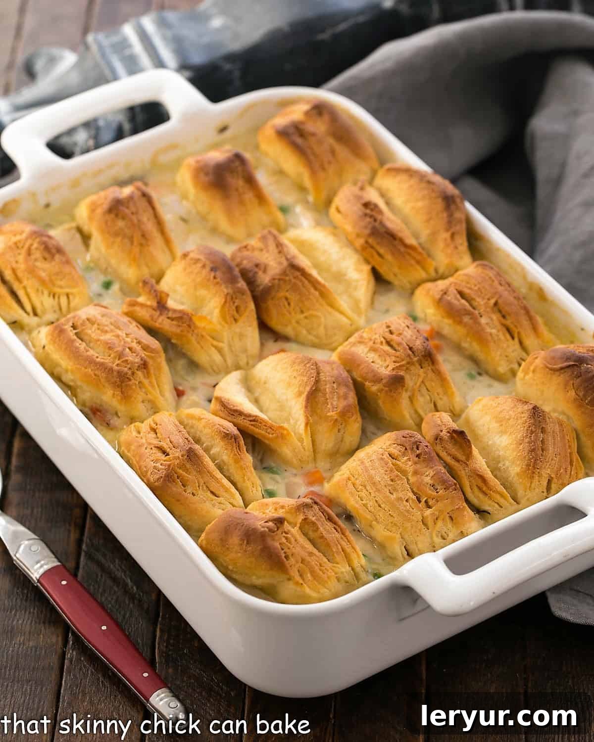 Chicken Pot Pie Casserole with Flaky Biscuits - A Hearty Family Meal A white casserole dish filled with golden-brown chicken pot pie, generously topped with an array of perfectly baked, flaky butterflake biscuits.