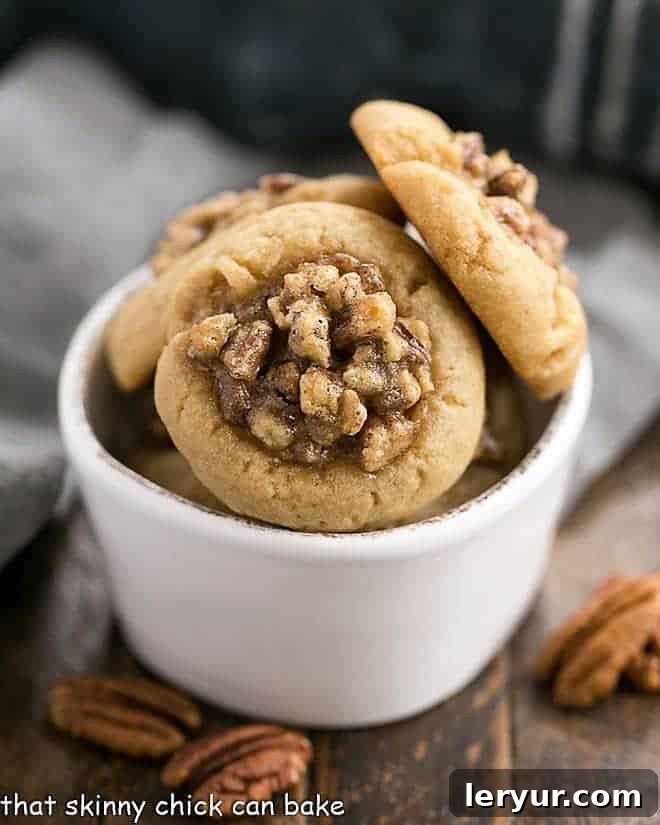 Pecan pie thumbprint cookies artfully arranged in a white bowl, showcasing their golden-brown edges and rich, textured filling.