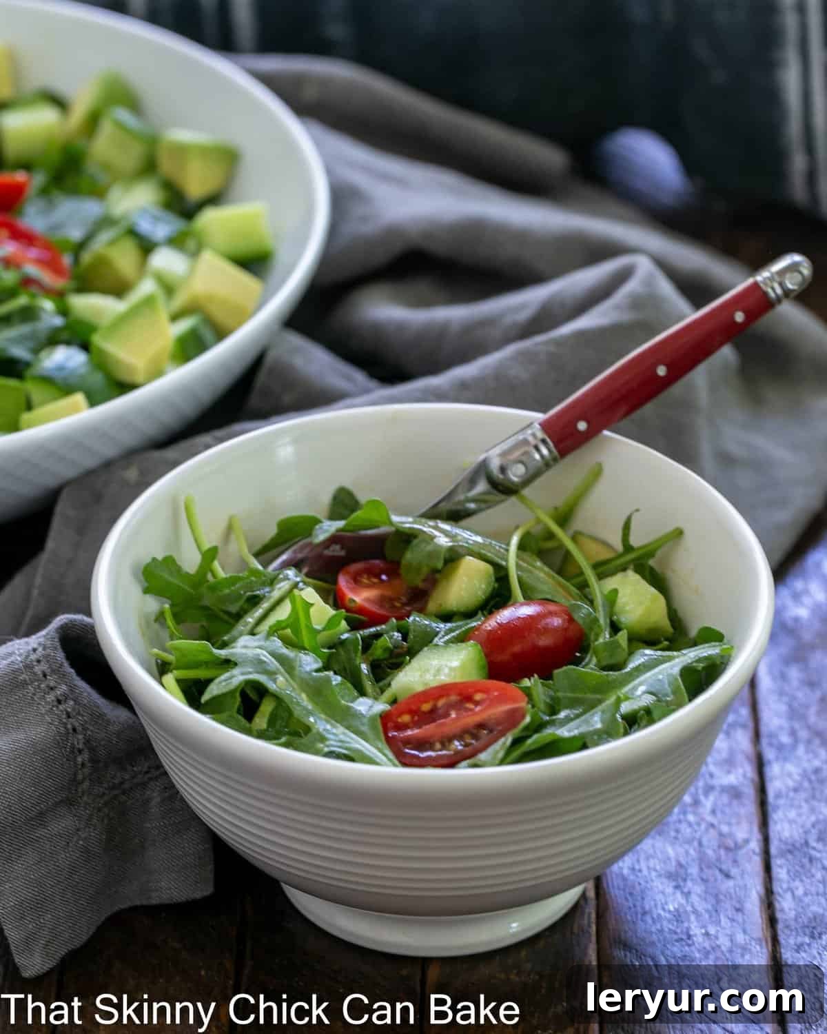 Bright Arugula Salad 3 A vibrant bowl of arugula salad with a red-handled fork resting in front, showcasing fresh greens and colorful vegetables.