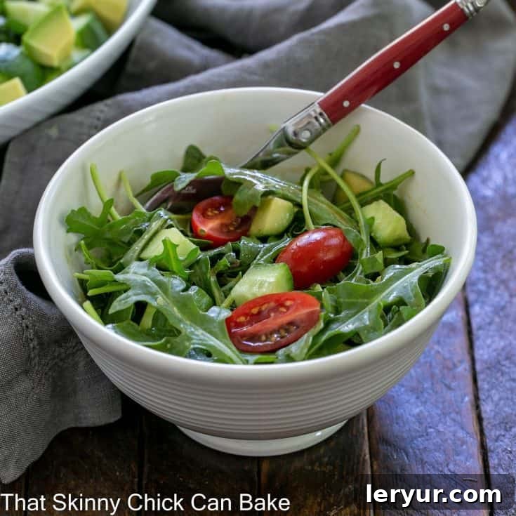 Simple arugula salad in a small white bowl with a fork, ready to be served.