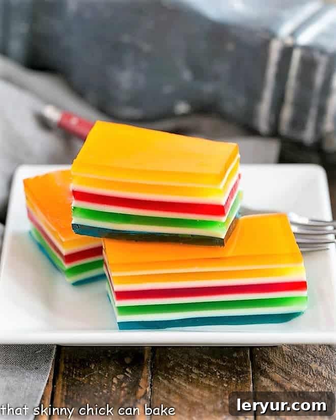 Vibrant Layered Jello Rainbow Salad - a special jello treat that can be made in many color combinations to celebrate any holiday or special occasion! Layered Jello Rainbow Salad squares stacked on a white plate, showcasing vibrant colors.