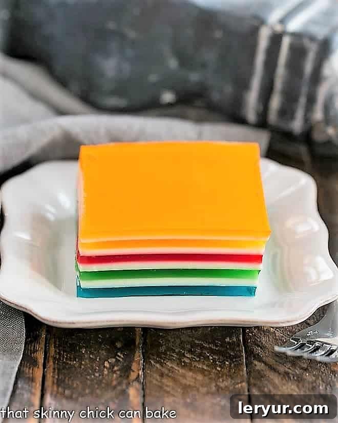 A fun vibrant Ribbon Jello Recipe is a wonderful project for kids and makes a special treat for any meal or holiday! A square of Jello Rainbow Ribbon Salad on a square white plate, ready to be served.