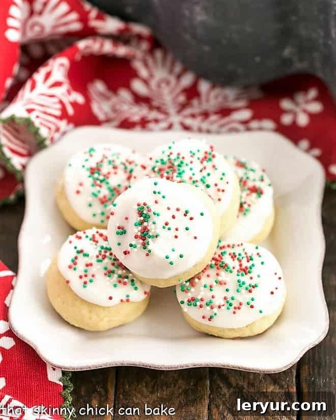 Tender, irresistible Frosted Italian Ricotta Cookies - an Italian Christmas cookie that's too delicious not to make all year long!! #cookies #holidaycookies #Christmascookies #Italian #cookieexchange #sugarcookies #thatskinnychickcanbake A square white plate holding a pile of delectable frosted Italian Ricotta Cookies, each topped with colorful sprinkles.