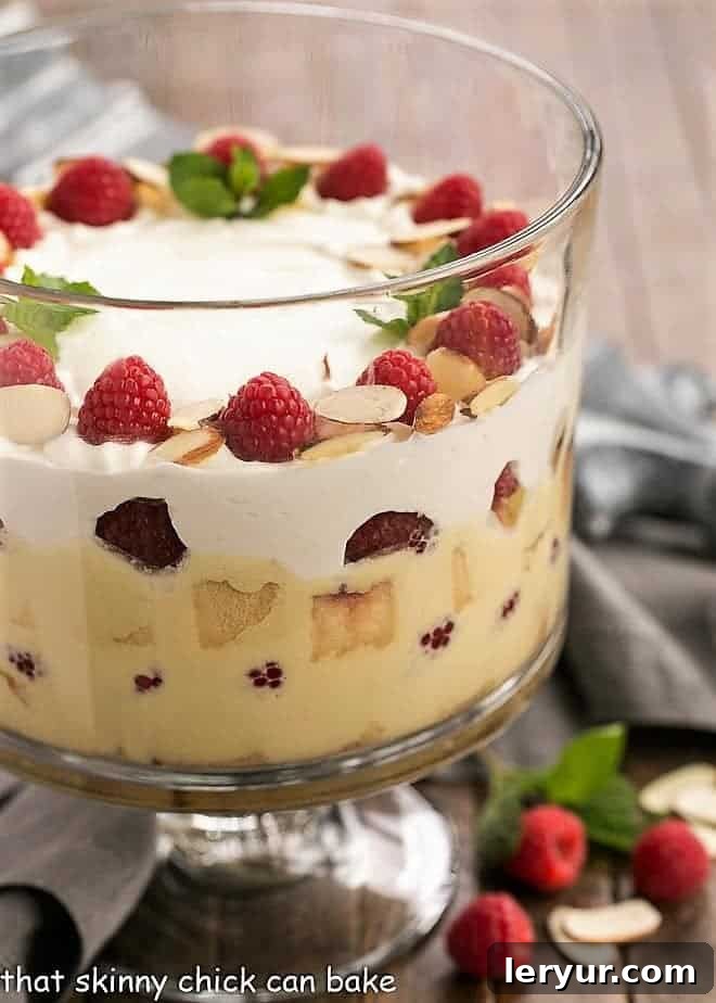 Traditional English Trifle side view in a glass trifle bowl, showcasing layers of cake, creme anglaise, and raspberries.