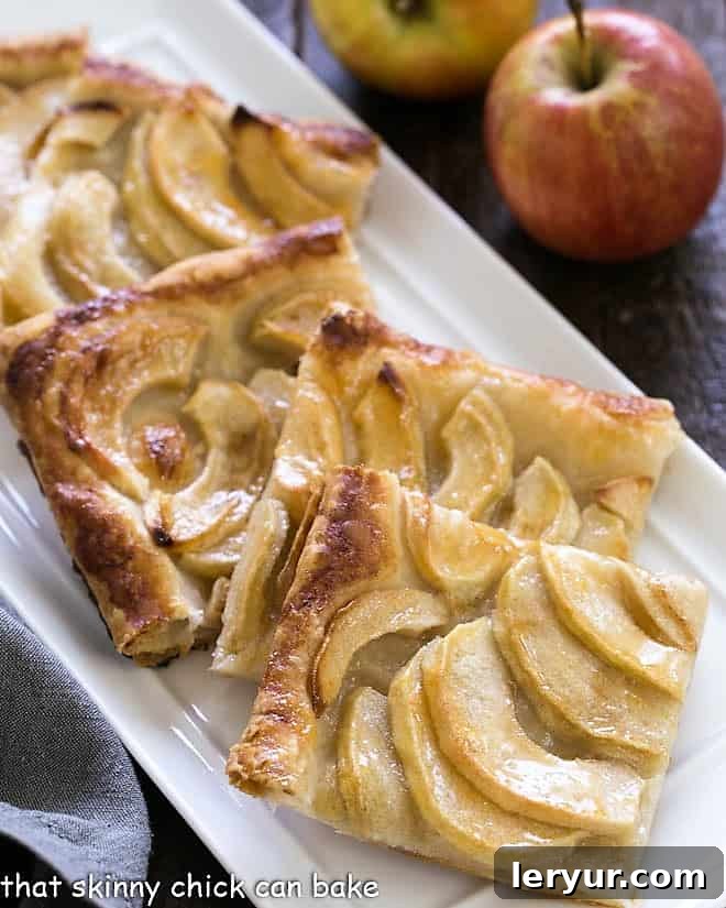 Slices of golden French Apple Tart on a pristine white ceramic tray, showcasing perfectly arranged apple slices and a flaky puff pastry crust.