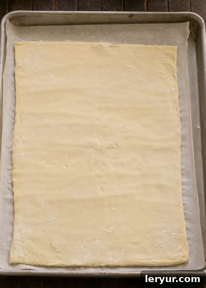 Sheet of defrosted puff pastry on a baking sheet, ready for apple arrangement.