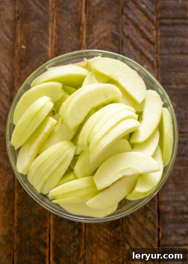 Chef's knife slicing a peeled and cored apple into thin, uniform pieces.