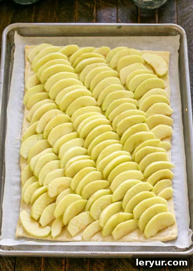 Thinly sliced apples meticulously arranged in overlapping rows on a sheet of puff pastry.