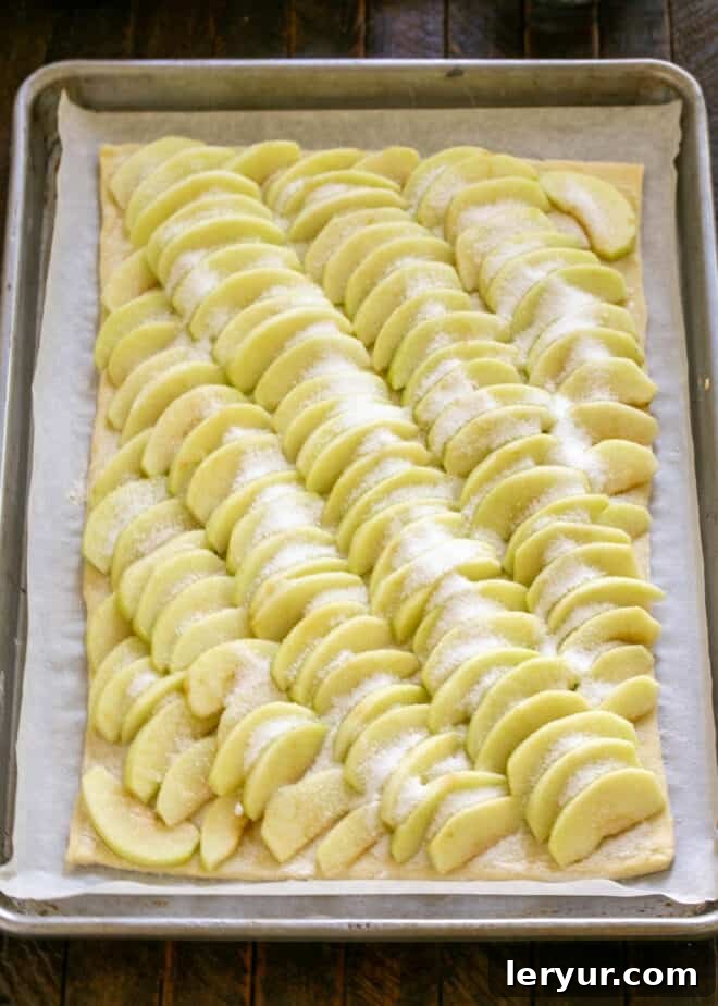 Puff pastry tart with arranged apples, sprinkled with sugar and dotted with small cubes of butter.