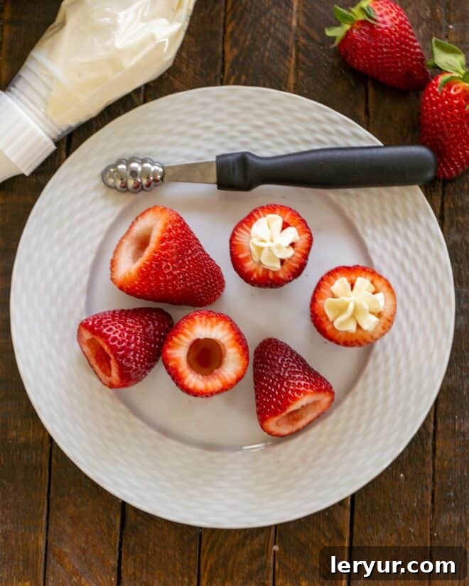 Overhead view of cored strawberries and two filled strawberries on a white plate, demonstrating the hollowing and piping process.