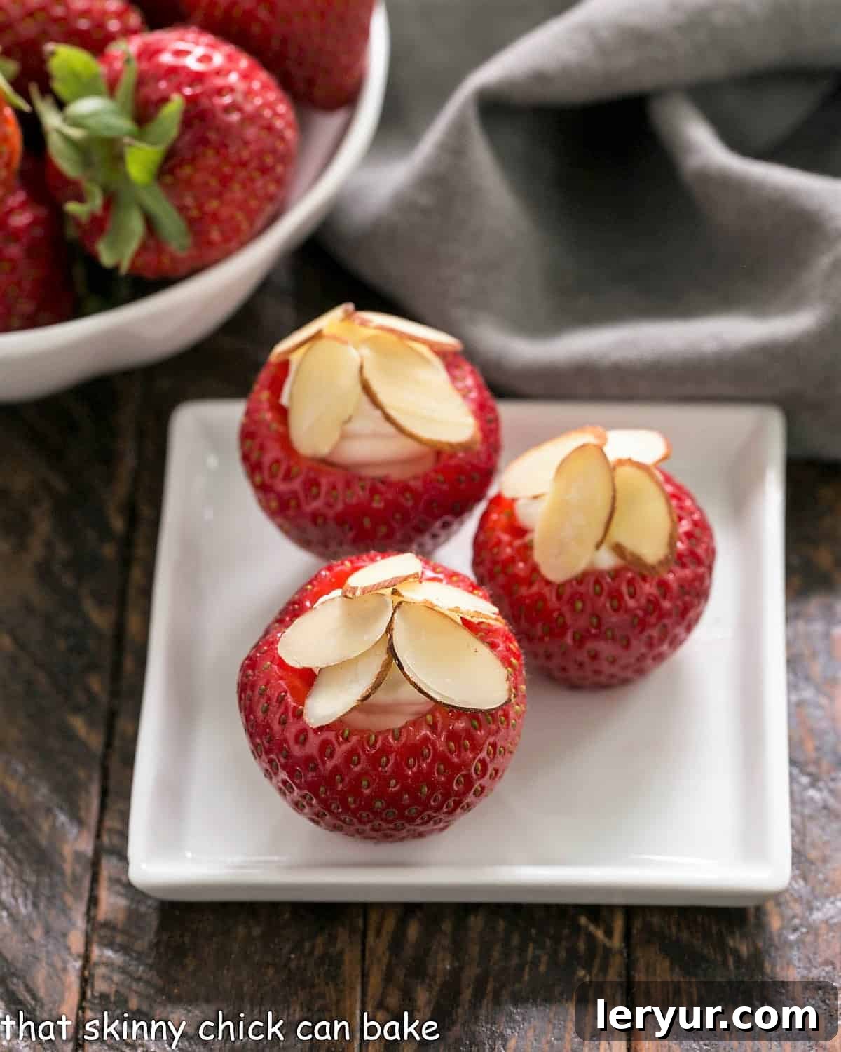 Three perfectly stuffed strawberries arranged on a square white plate, highlighting their vibrant color and creamy filling.