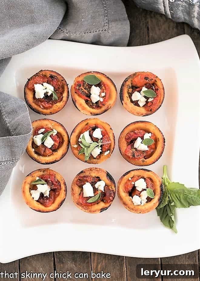 Buttery, cheesy pastry crusts filled with herb marinated tomatoes and feta cheese for an irresistible appetizer Cheese Straw Tomato Tartlets arranged neatly on a white rectangular serving tray.