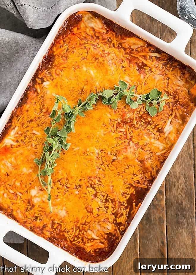 Easy Turkey Enchilada Casserole - super simple casserole with tortillas, turkey, enchilada sauce and cheese for a warm, comforting meal! Rich and cheesy Turkey Enchilada Casserole in a white baking dish, garnished with fresh oregano
